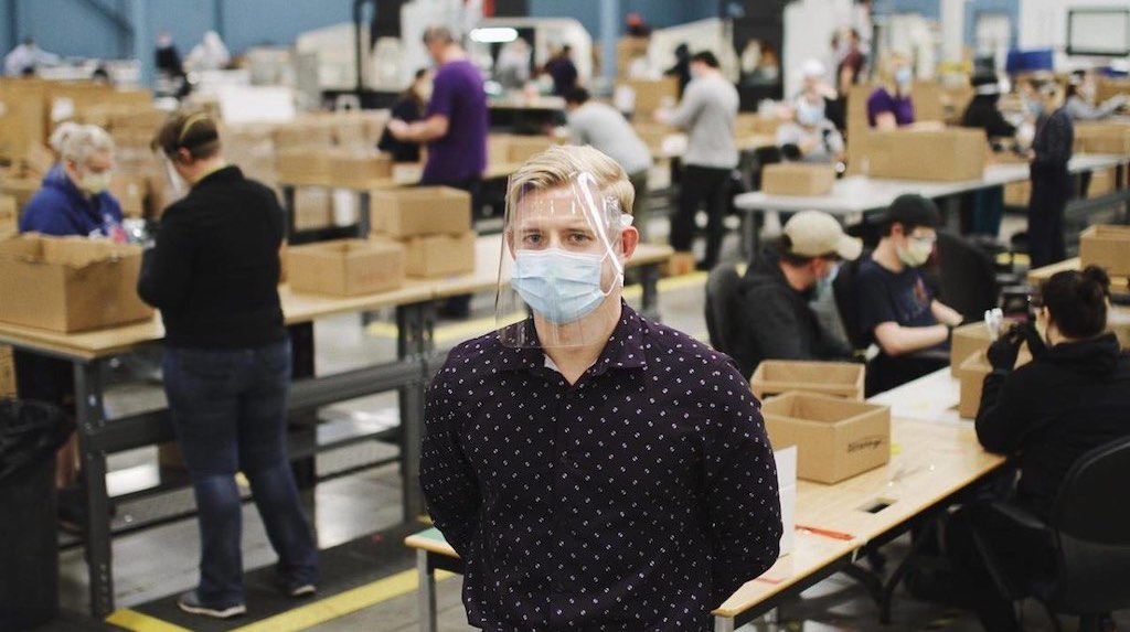A man standing in a warehouse wearing a face mask and face shield